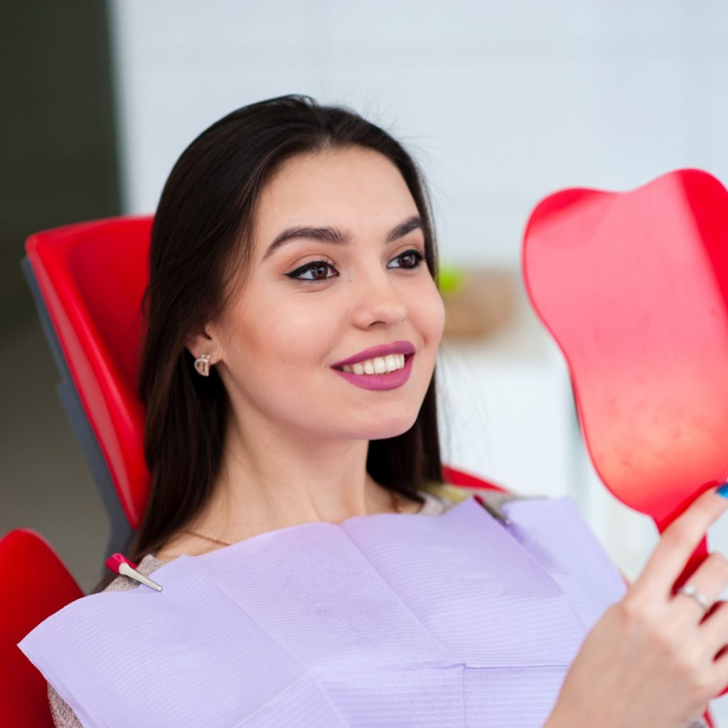Smiling woman checking her teeth in a tooth-shaped mirror