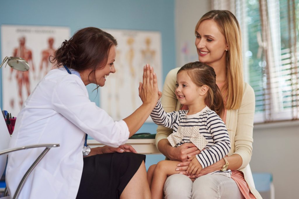 Dentist giving a young girl a high five while her mother holds her